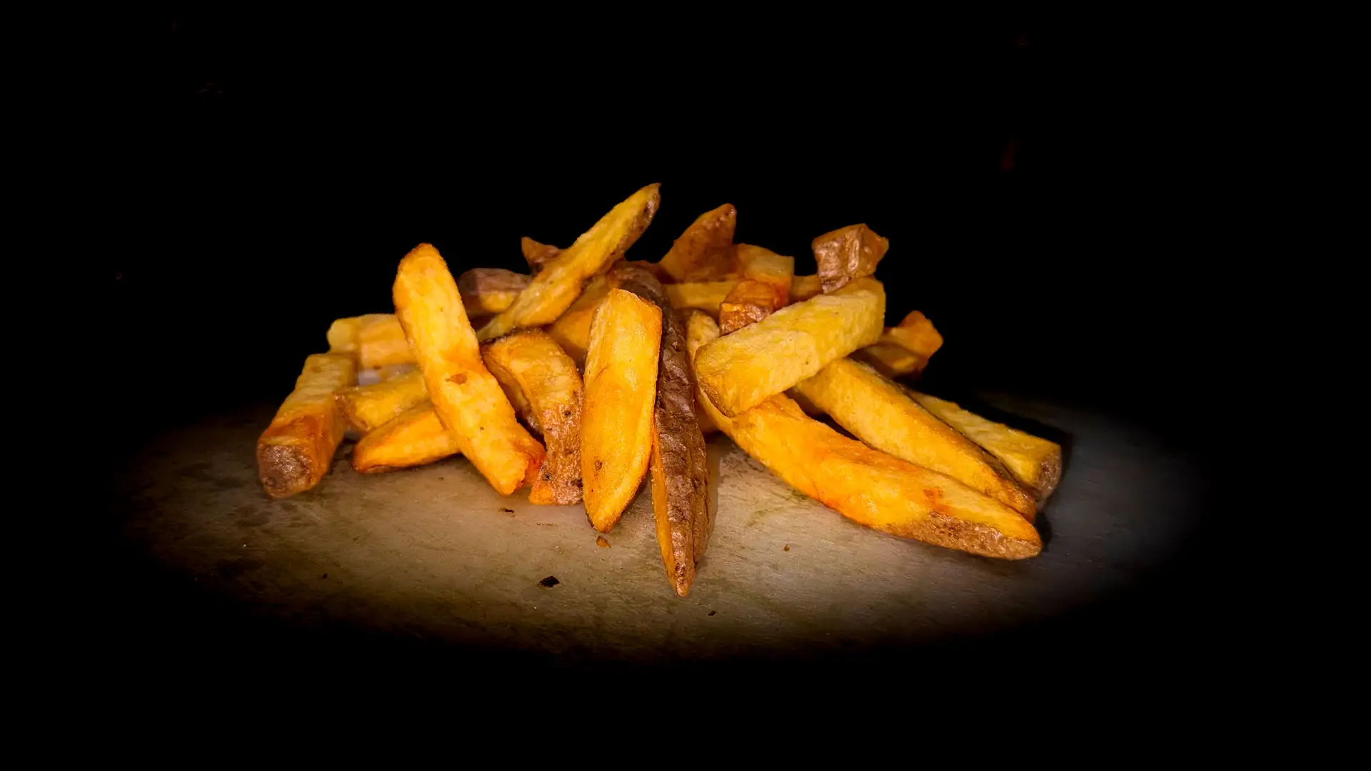 Goudbruine ambachtelijke frietjes op een donkere achtergrond, gepresenteerd als smakelijke snack van de FrietVrienden